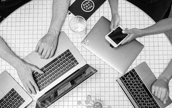 An overhead black and white view of several team members working on laptops and a smartphone around a tiled table, representing collaborative business strategy.